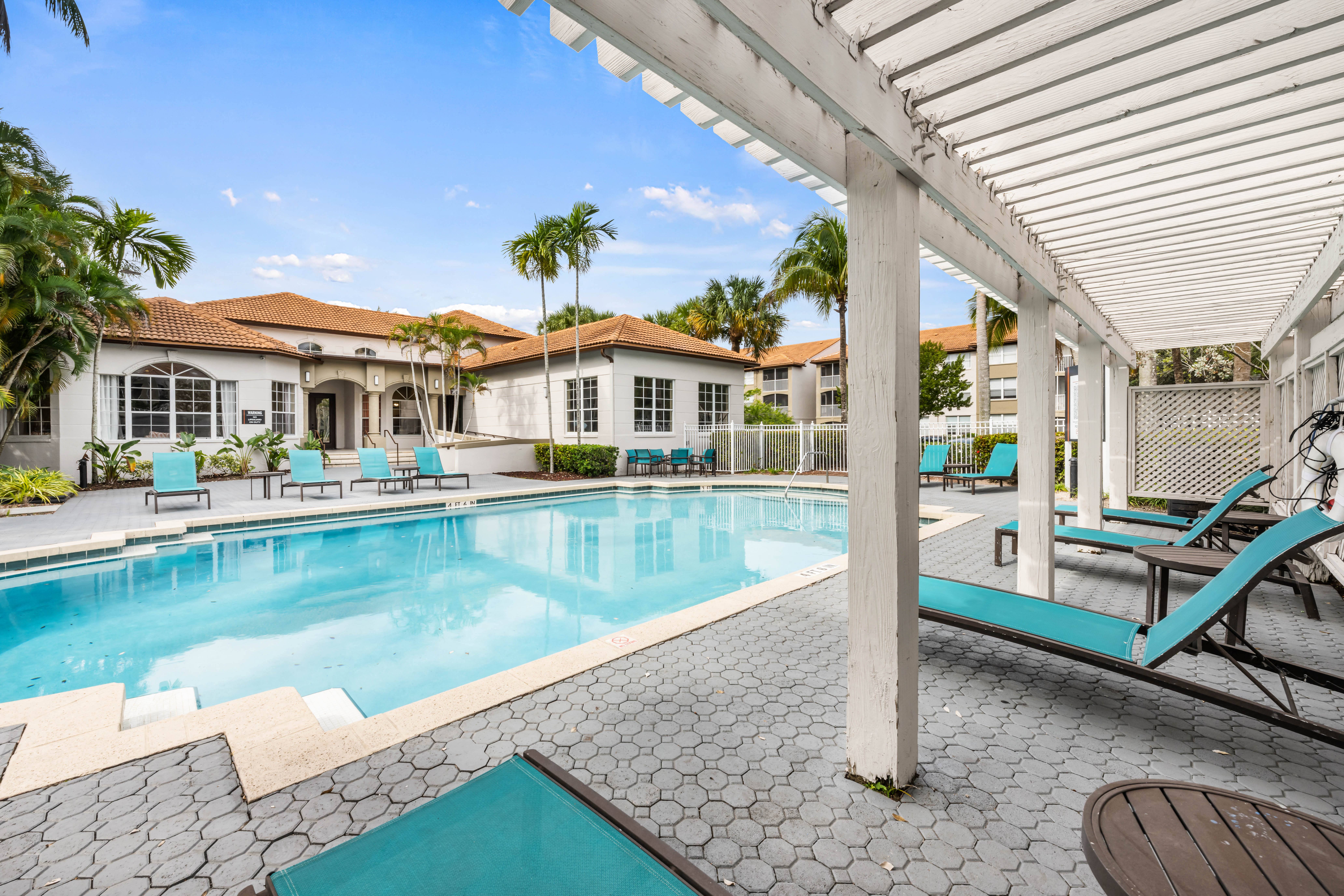 A pool area with a white pergola and blue lounge chairs.